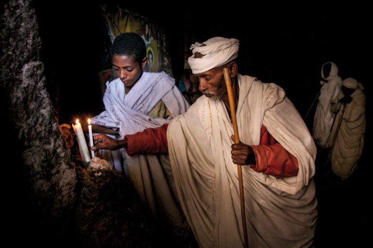 Al llegar la noche, los peregrinos encienden sus velas, creando un ambiente místico e irreal. Los rostros se iluminan bajo la tenue luz dorada y, entre luces y sombras, se teje un entramado de misterio.